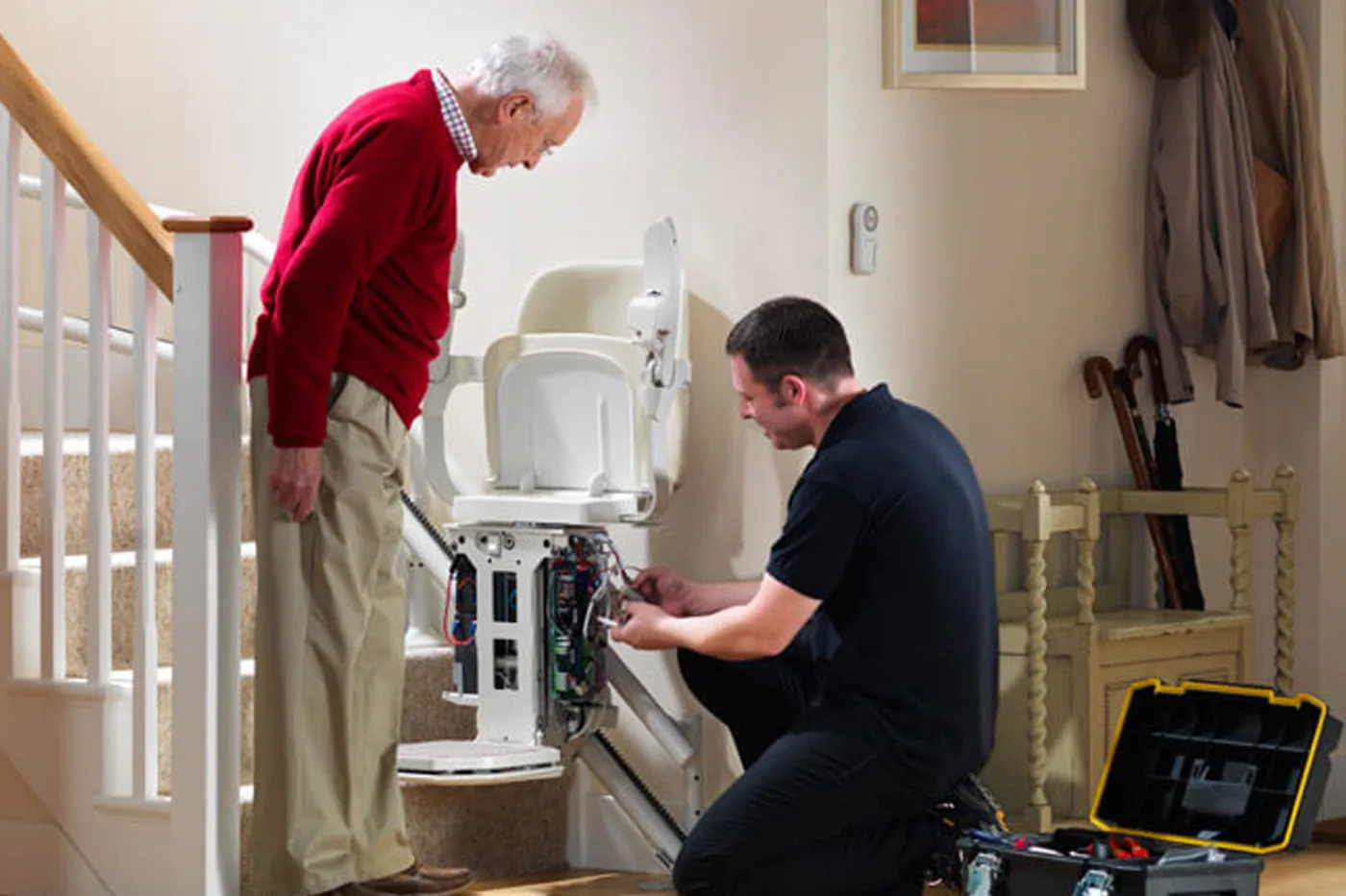 A customer watches a Mobility Minder engineer work on his stairlift at the foot of the stairs