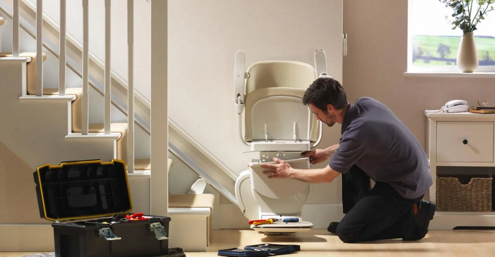 A Mobility Minder engineer kneeling at the foot of the stairs, servicing a stairlift seat
